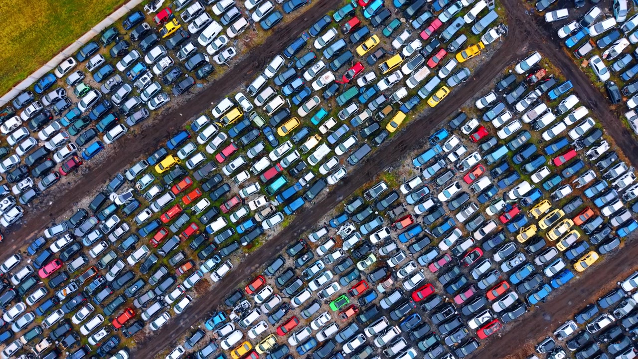 Composizione aerea diagonale di veicoli vecchi stipati densamente. Inquadratura diagonale dall'alto di numerose auto colorate disposte in file geometriche in uno sfasciacarrozze