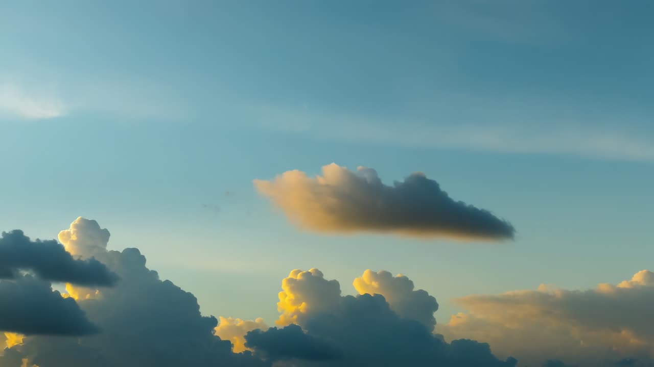 Drifting cumulus cloud cluster catching golden sunlight in open sky as sun sets, forming silhouette