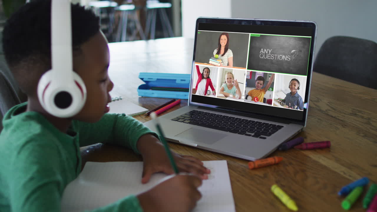 Schoolboy using laptop for online lesson at home, with diverse teacher and class on screen