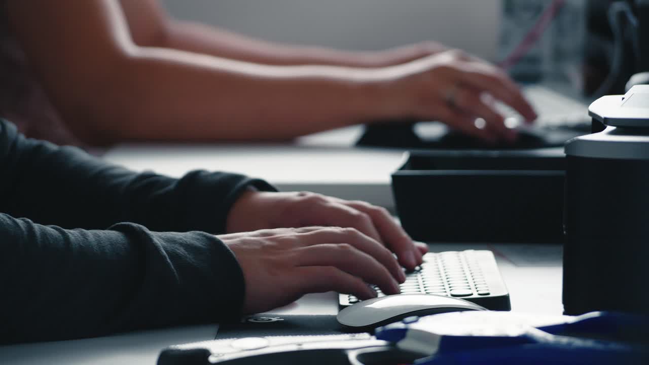 Close-up of male hands typing quickly on a black computer keyboard in a dimly lit modern office. Professional programming or data entry work in a tech startup environment