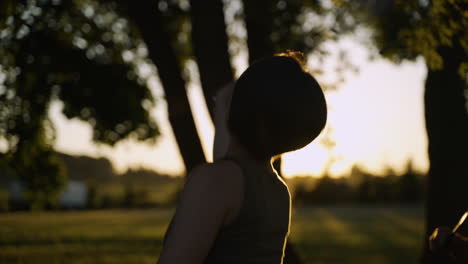 woman with short hair in a tank top plays badminton in a field as the sun sets in the background