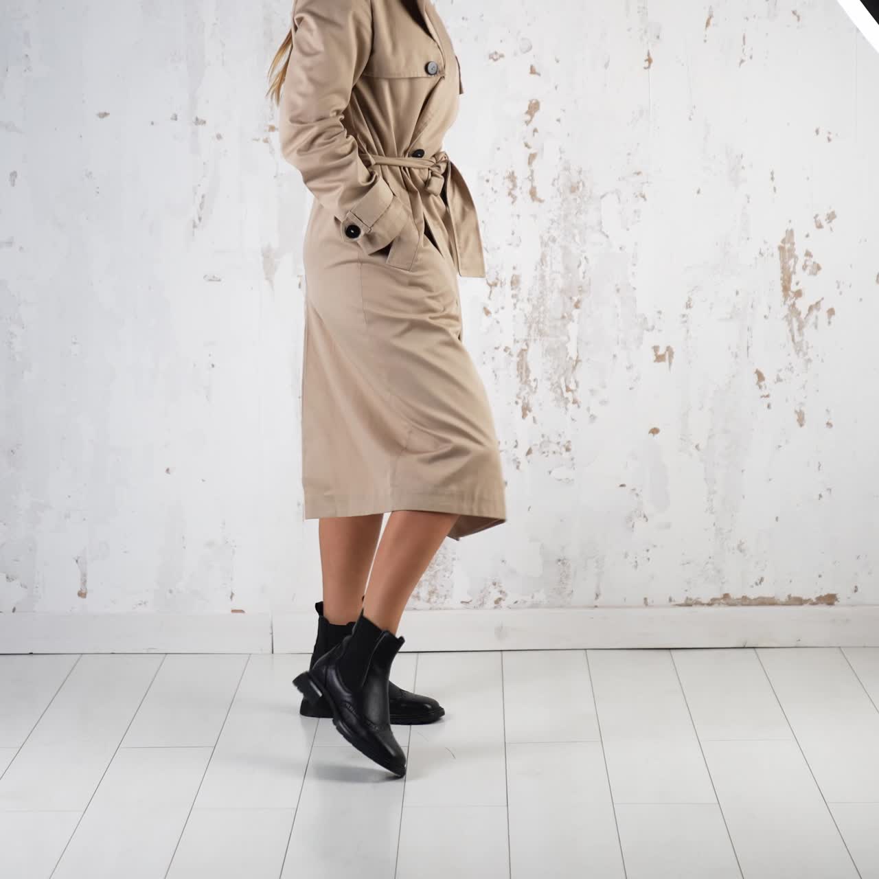 Modern clothes and stylish footwear demonstration. Model wearing beige coat and black tractor boots posing in the studio