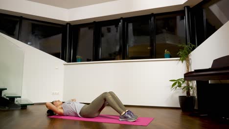 Woman doing crunches on a pink yoga mat in a home interior at night, low angle view