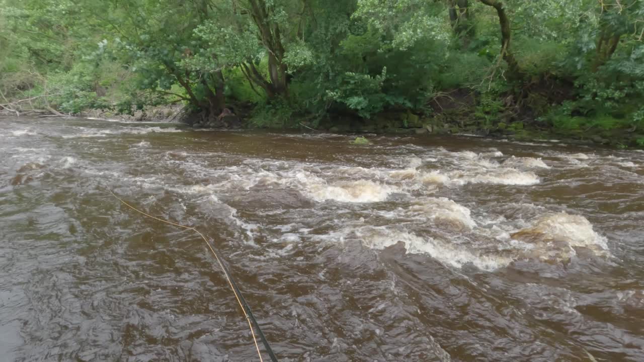 POV shot of a fly fishing rod being casted into a fast-moving brown river