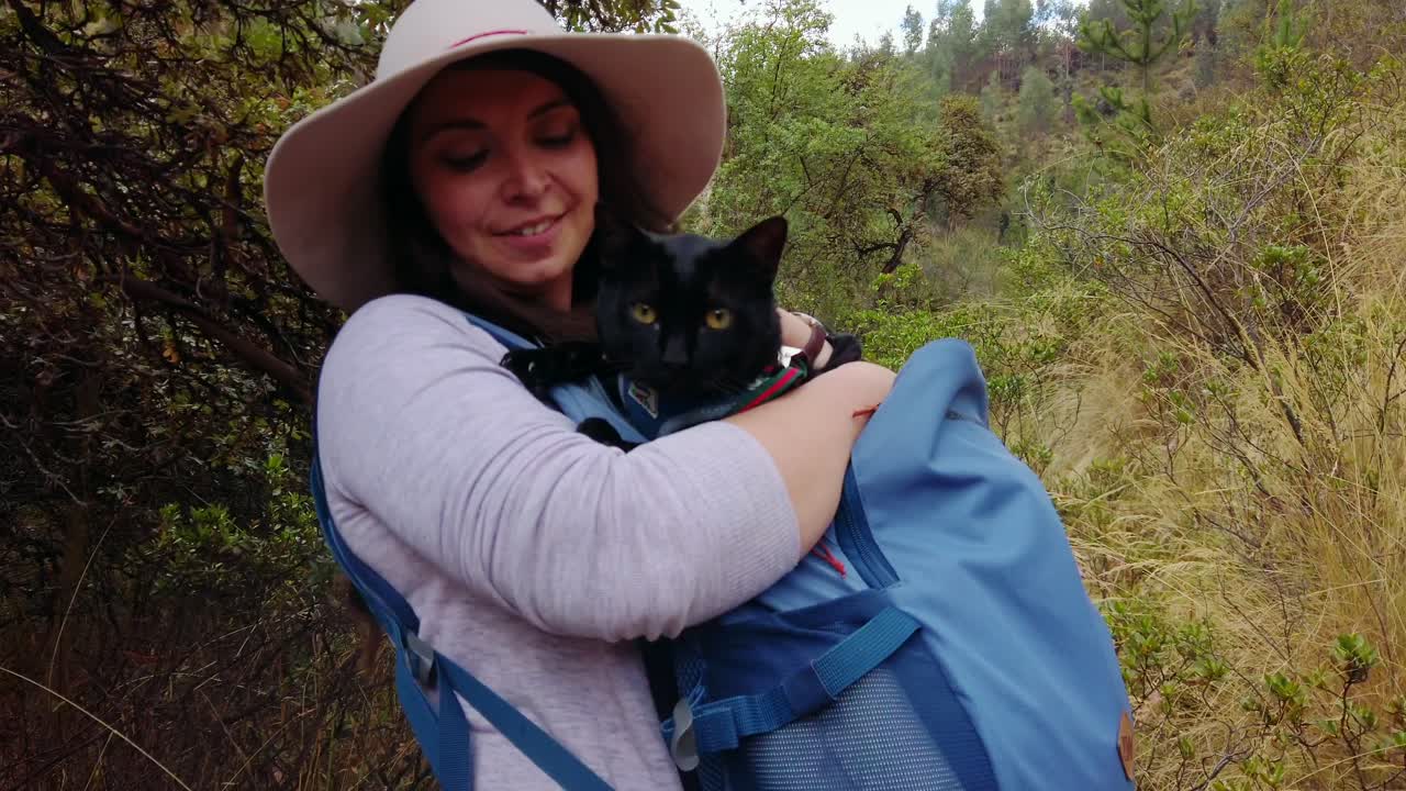 Dolly-in approaching shot of a woman traveler carrying a black cat in her backpack on a historical trail near Cusco, Peru