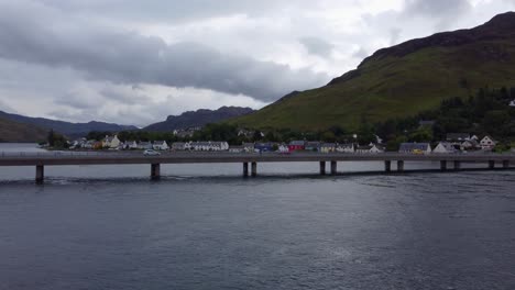 Cars-driving-over-bridge-near-Eilean-Donan-Castle-in-Dornie,-West-Coast-of-Scotland,-Scottish-Highlands---Aerial-Drone-4k-HD-Footage-Pan-Right