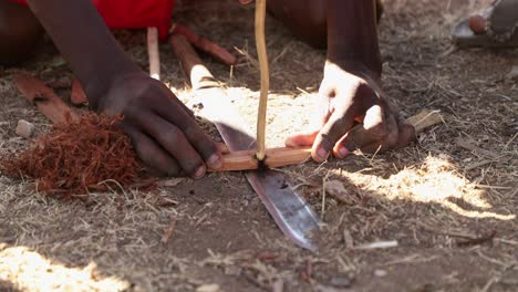 maasai man making fire by rubbing two sticks together to create friction