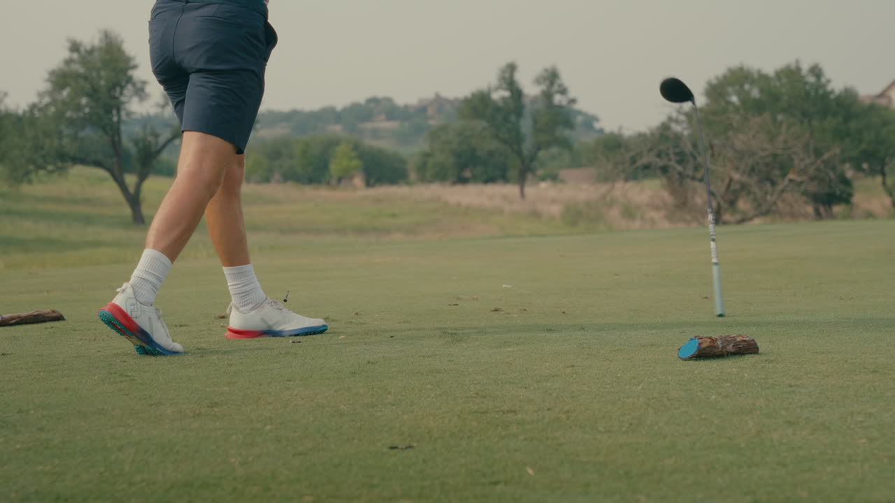 Waist-down slow motion shot of a male golfer hitting a poor drive off the blue tees. In frustration, the club is released during his follow-through, capturing real emotion and raw course energy.
