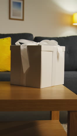 vertical video of present in gift wrapped box decorated with ribbon on table in lounge