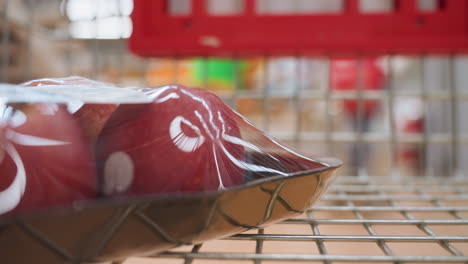 a hand placing a package of apples in a shopping trolley, captured in a dynamic mall environment. this immersive view highlights the act of grocery shopping with a handheld camera