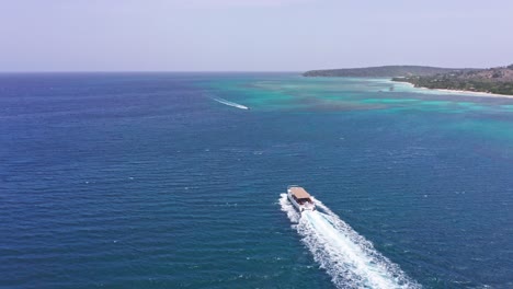 Ferry-Con-Turistas-Navegando-En-El-Mar-Azul-Con-Retrolavado-En-Playa-La-Ensenada,-República-Dominicana