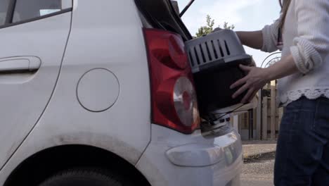 Woman-putting-pet-carrier-into-car-boot-wide-shot