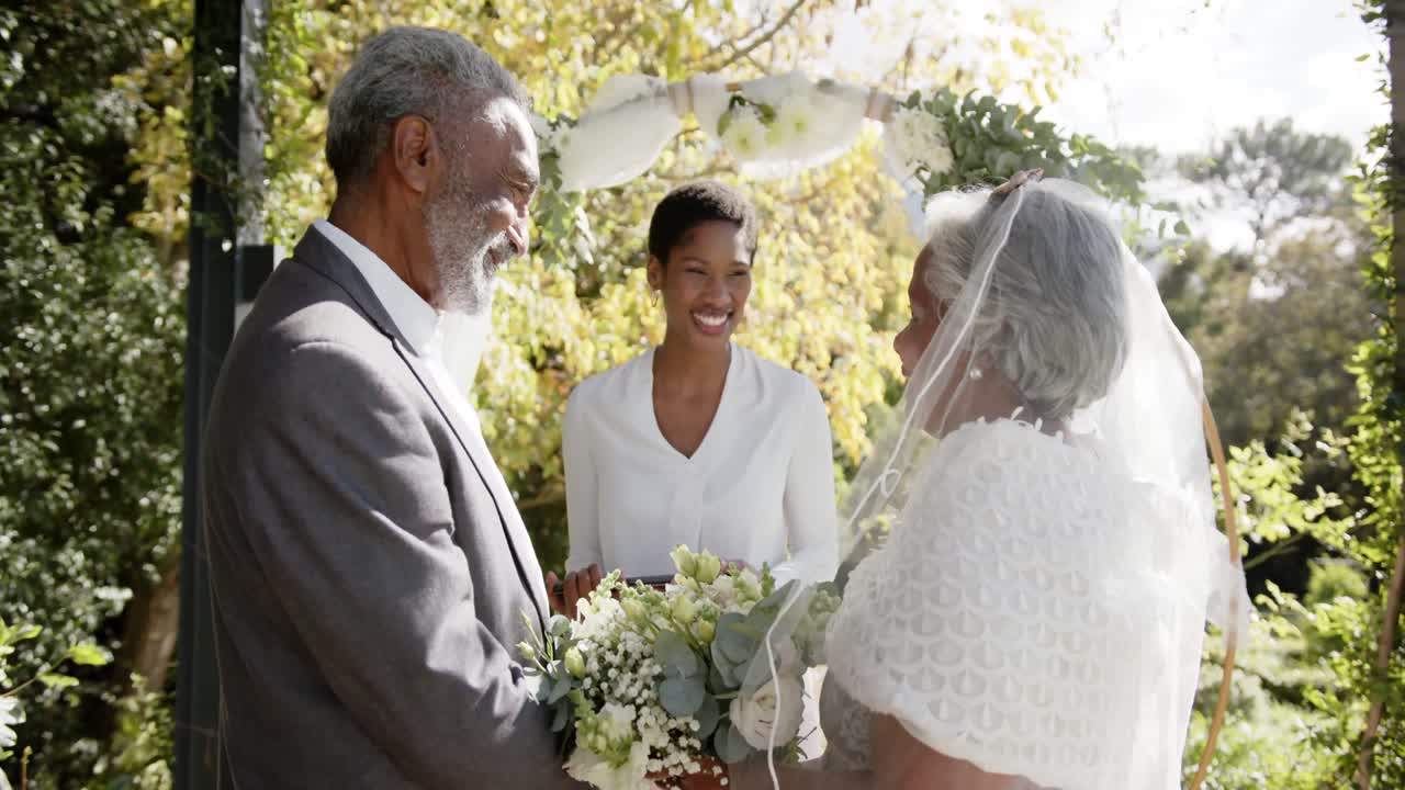 Donna afroamericana che celebra la cerimonia di matrimonio di una coppia birazziale anziana in giardino, in slow motion.