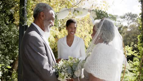 Mujer-Afroamericana-Oficiando-Ceremonia-De-Boda-De-Una-Pareja-Birracial-Mayor-En-El-Jardín,-Cámara-Lenta