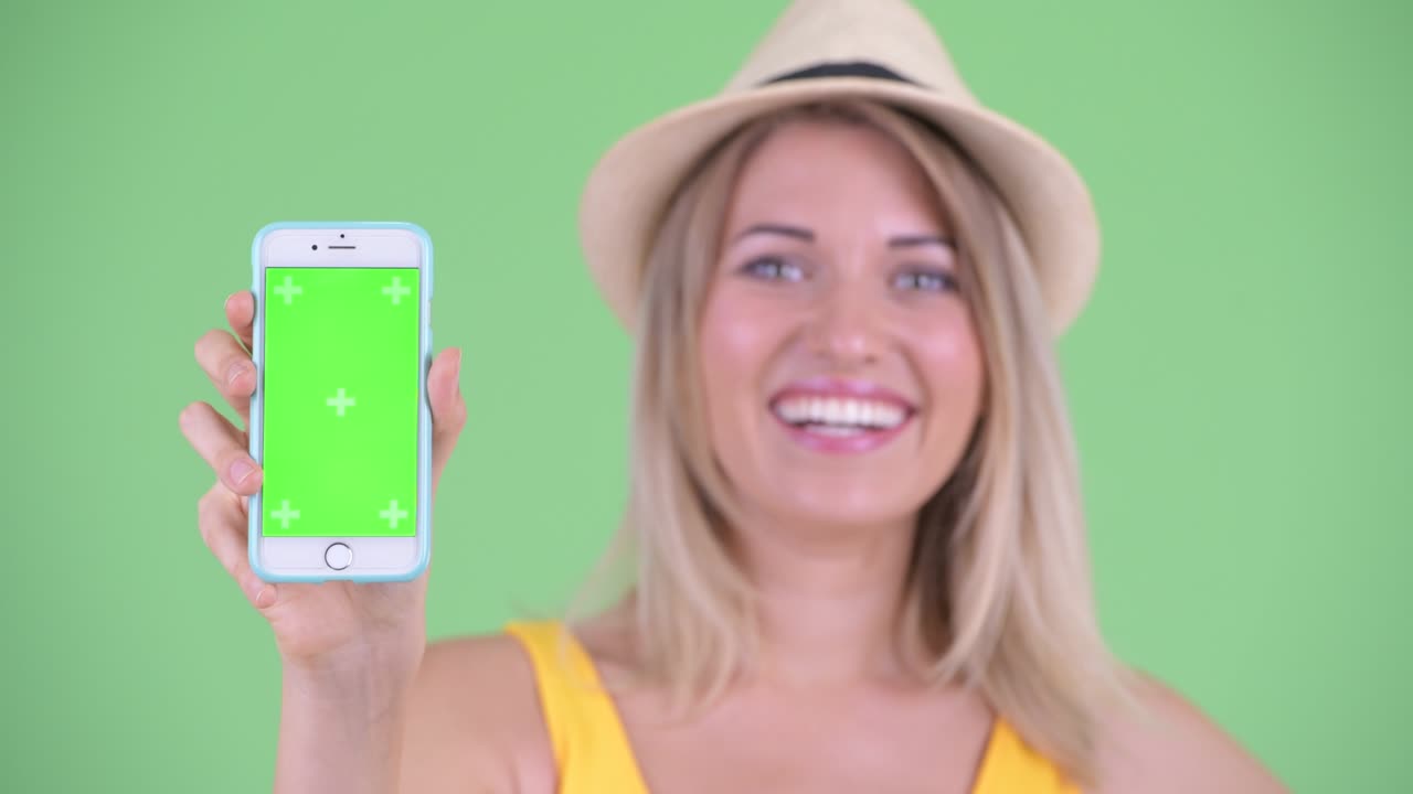 fotografía de estudio de una joven turista sonriendo y mostrando un teléfono móvil con espacio de copia contra un fondo verde