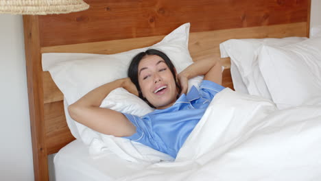 waking up, woman stretching in bed wearing blue pajamas, feeling refreshed, at home