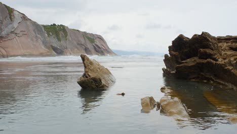 low angle water ripples shimmer shine around exposed sharp pieces of rock, itzurun beach