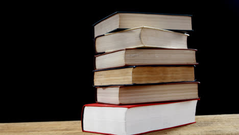 Animation-of-blue-microscope-over-stack-of-books-on-wooden-desk,-on-black-background