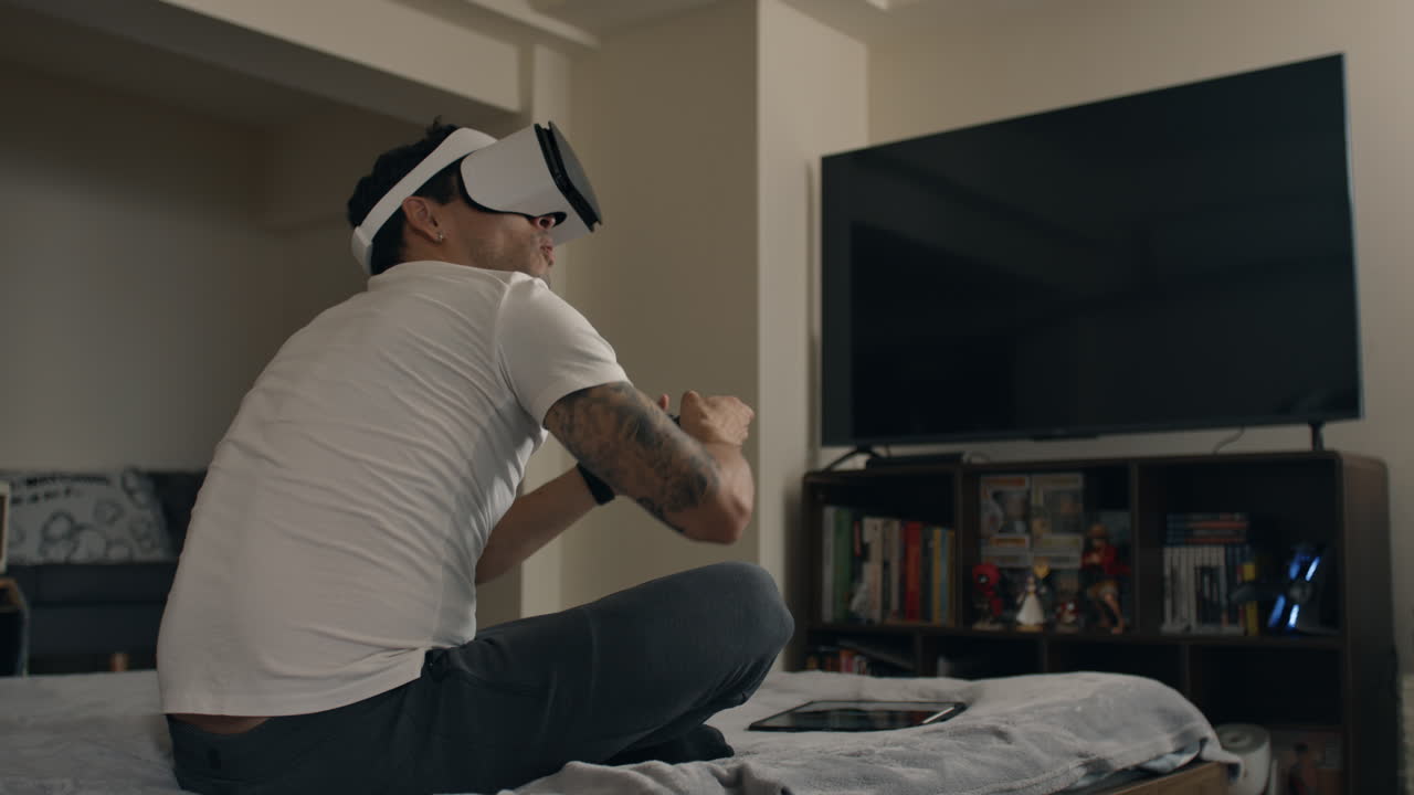 Man uses VR headset and controller for intense gaming session while sitting on bed at home