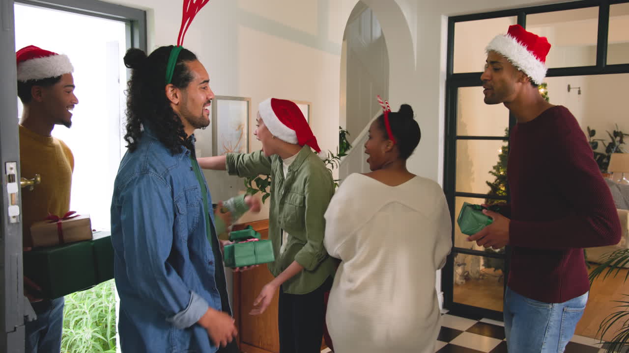 Young diverse friends exchanging gifts at home, wearing Santa hats, celebrating Christmas