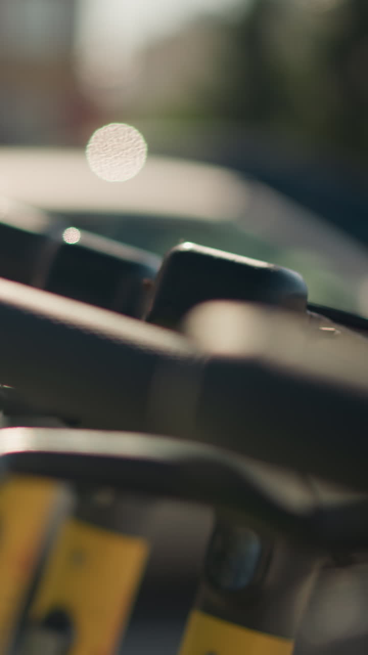 primer plano del manillar de un patinete a la luz del sol, flota de alquiler alineada en el bordillo de la ciudad durante la hora dorada, bokeh con poca profundidad de campo que destaca la palanca de freno y el agarre texturizado, un viajero desbloquea el patinete, entrega