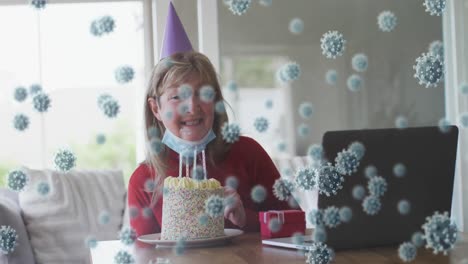 animación de células del virus covid-19 sobre una mujer caucásica mayor que usa una máscara facial celebrando su cumpleaños