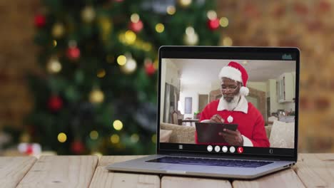 Hombre-Afroamericano-Mayor-Disfrazado-De-Santa-En-Videollamada-En-Computadora-Portátil,-Con-árbol-De-Navidad