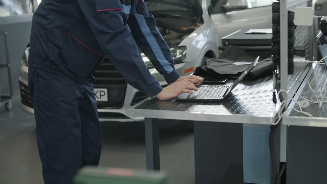 차고에서 노트북을 사용하여 자동차를 수리하는 기계공