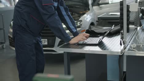 mechanic working on a car using a laptop in a garage