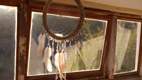 dreamcatcher with feathers hanging in sunlight by a rustic window