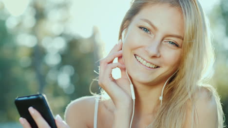 Eine-Junge-Frau-Mit-Kopfhörern-Hört-Musik-Mit-Einem-Smartphone,-Die-Sonne-Beleuchtet-Sie-Wunderschön