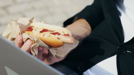 man eating hot dog while working on laptop