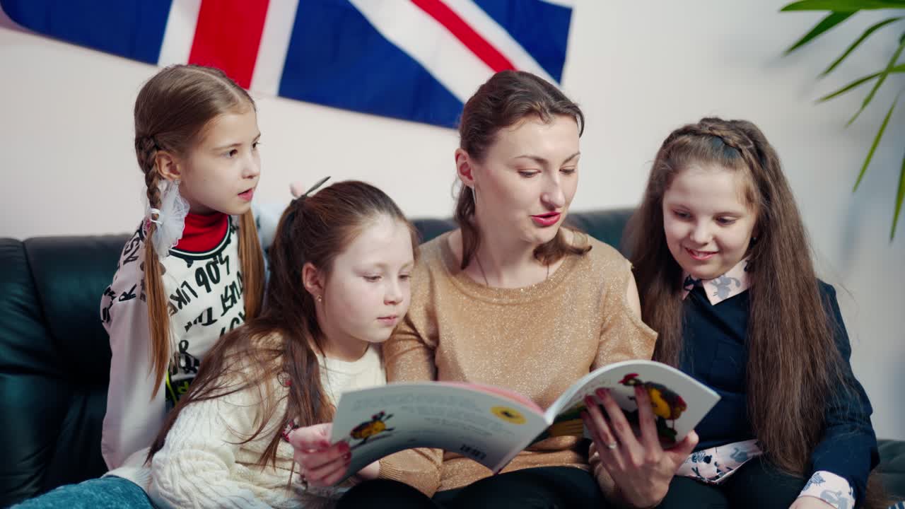 Elementary education. Woman teacher sitting together with little students on the couch and reading a book. Schoolgirls talk with a teacher.