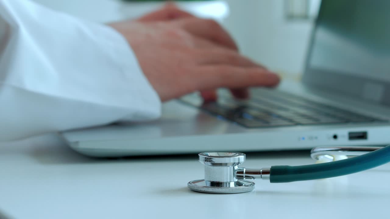 Concept Medicine, the doctor works, the hands of a man in a white coat are printing text on Laptop, a fanendoscope on a white table