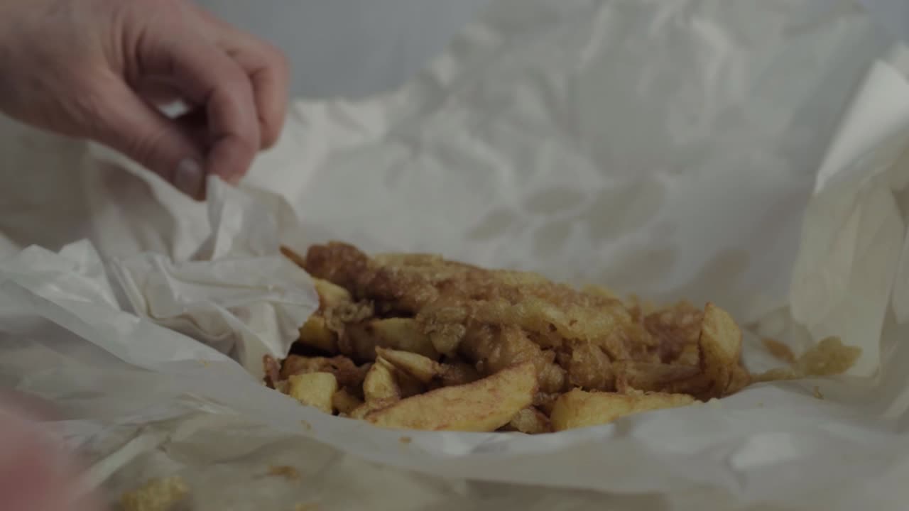 Hand unwrapping fish and chips side medium shot