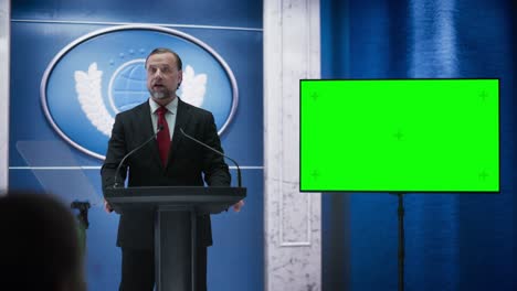 organization representative speaking at a press conference in government building with a green screen mock up on display. press officer delivering a speech at summit. minister speaking to congress.