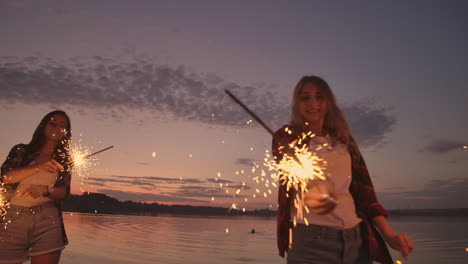 beautiful women in summer with sparklers dancing in slow motion on the beach at night