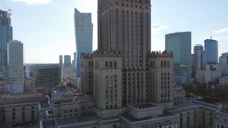 Aerial-footage-of-Palace-Of-Culture-in-Warsaw,-increasing-altitude-revealing-sun-over-the-top