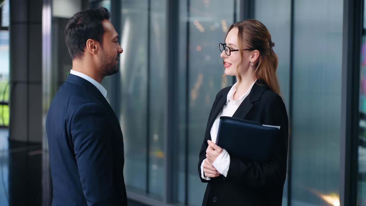 Business colleagues walk to center, man and woman, shaking hands in modern glass hallway, medium static