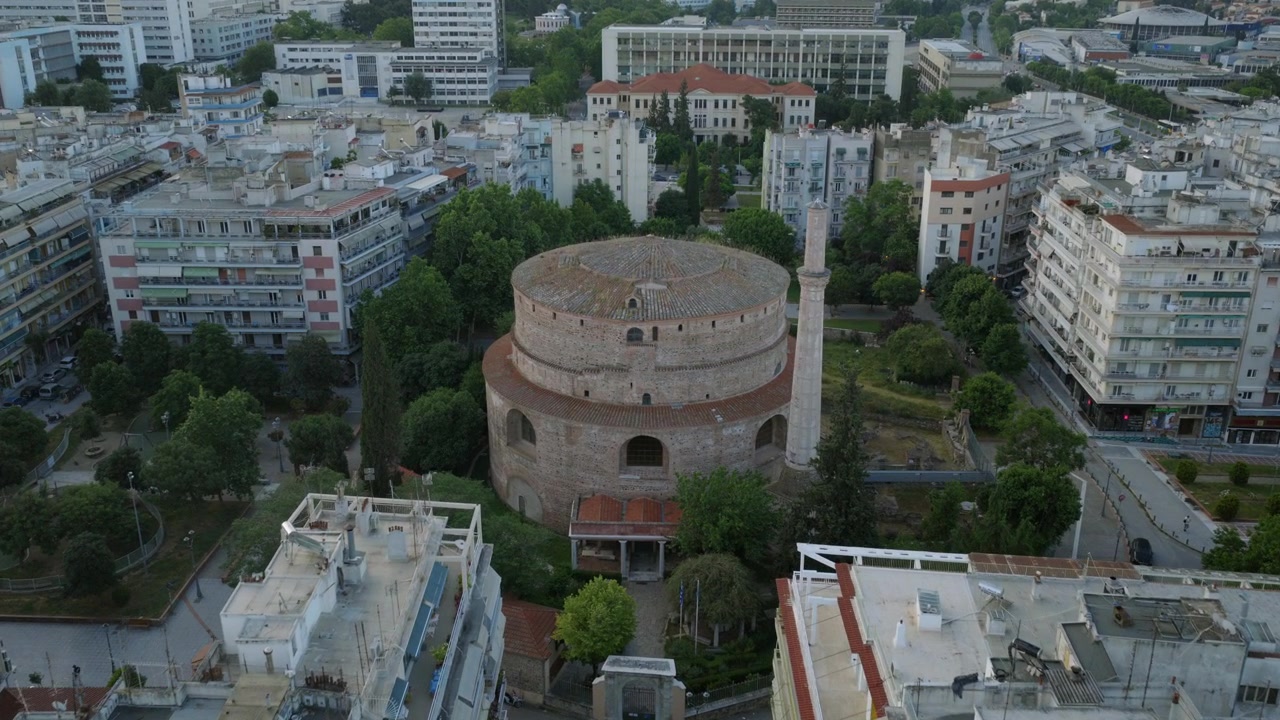 Veduta aerea lungo un viale alberato verso l'Arco di Galerio, un antico monumento romano incorniciato dal paesaggio urbano di Salonicco.