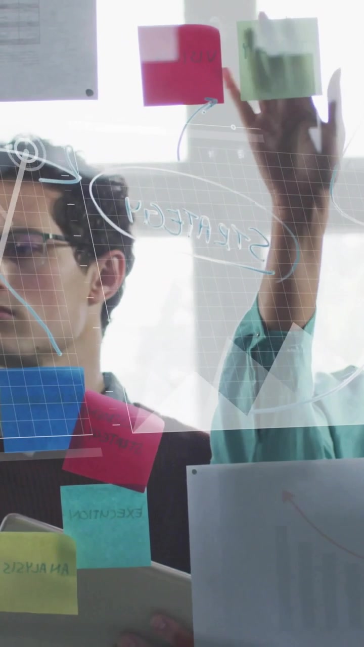 Video vertical: Equipo colocando notas en una tableta, mientras gráficos se muestran en un cristal, alineando el plan de negocios.