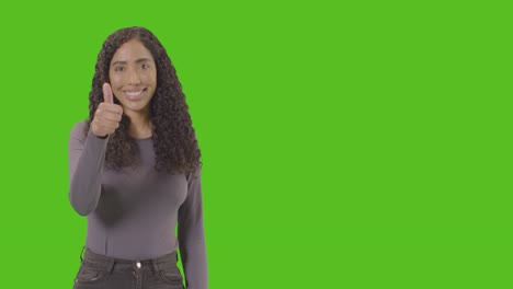 studio waist up shot of woman giving thumbs up sign against green screen
