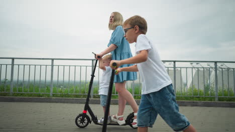 a mother is riding a scooter with her younger son, while the older child rides his scooter independently beside them