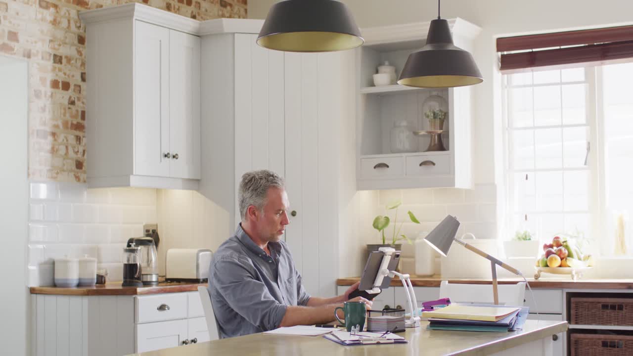 hombre caucásico feliz sentado en la mesa en la cocina, usando un teléfono inteligente