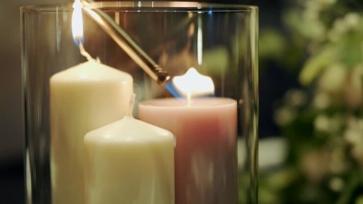 Candele bianche all'interno di un portacandele di vetro che vengono accese