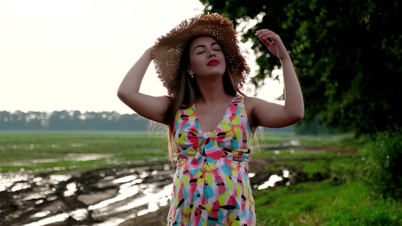 Chica embarazada camina por la carretera después de la lluvia con sombrero y vestido
