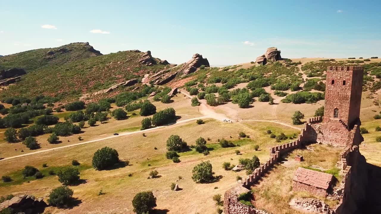 Aerial view of Castillo de Zafra, Spain, nestled amidst rugged terrain and lush greenery, showcasing its historic medieval architecture and natural surroundings under a vibrant blue sky
