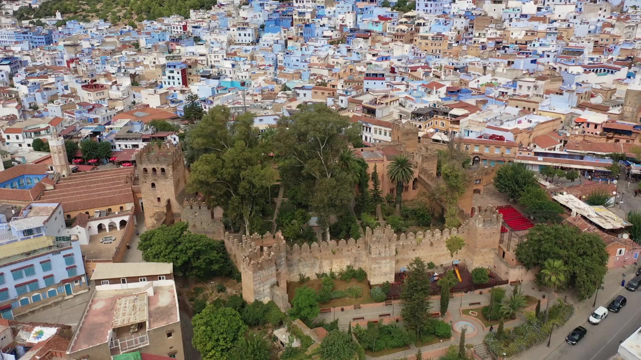 Lotniczy widok z drona na Chefchaouen, przedstawiający historyczną Kasbę otoczoną ikoniczną Niebieską Medyną. Położone w Górach Rif, to tętniące życiem górskie miasto jest jednym z najsłynniejszych kulturowych miejsc Maroka.