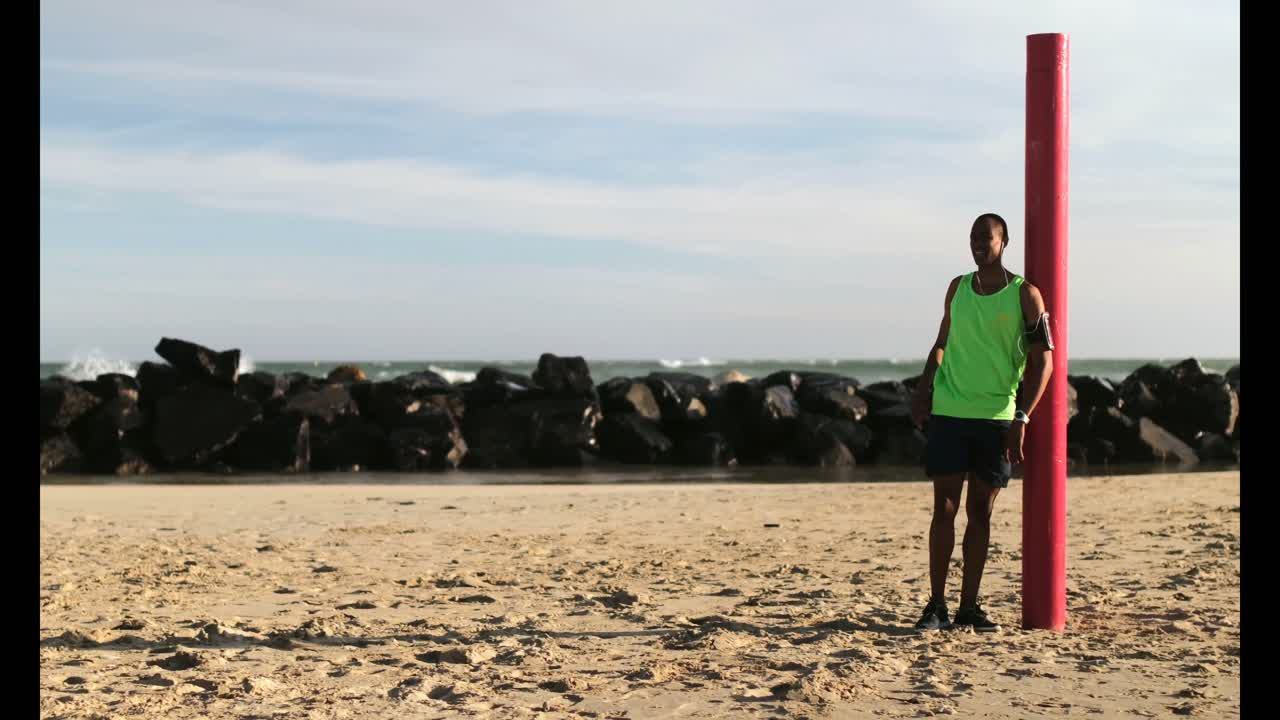 corredor masculino apoyado contra un poste en la playa al sol 4k