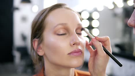 primer plano de la cara de un modelo durante el proceso de maquillaje. maestro de maquillaje aplicando sombras de ojos marrones claras. vista borrosa de blanco